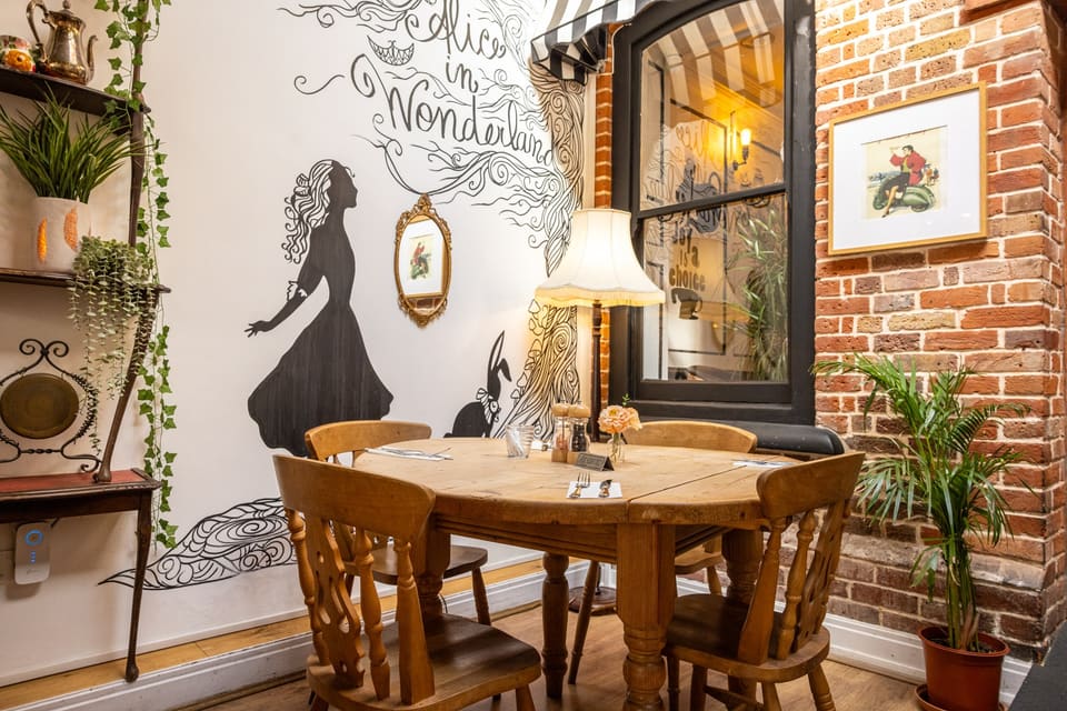 A round table in the corner under a mural of Alice and a striped awning window