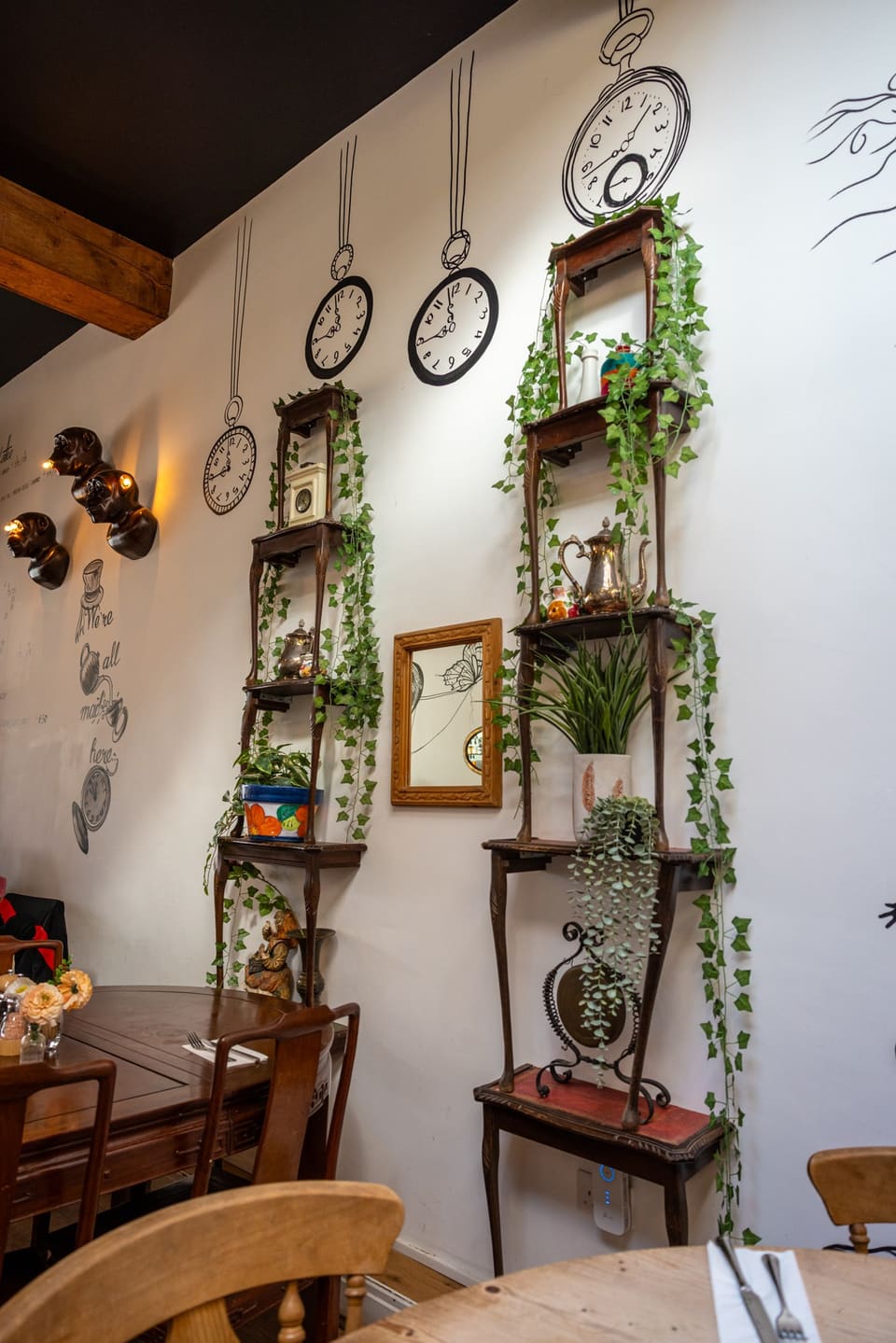 Wall of drawn pocket watches and clocks hanging on chains above shelves of plants and teapots