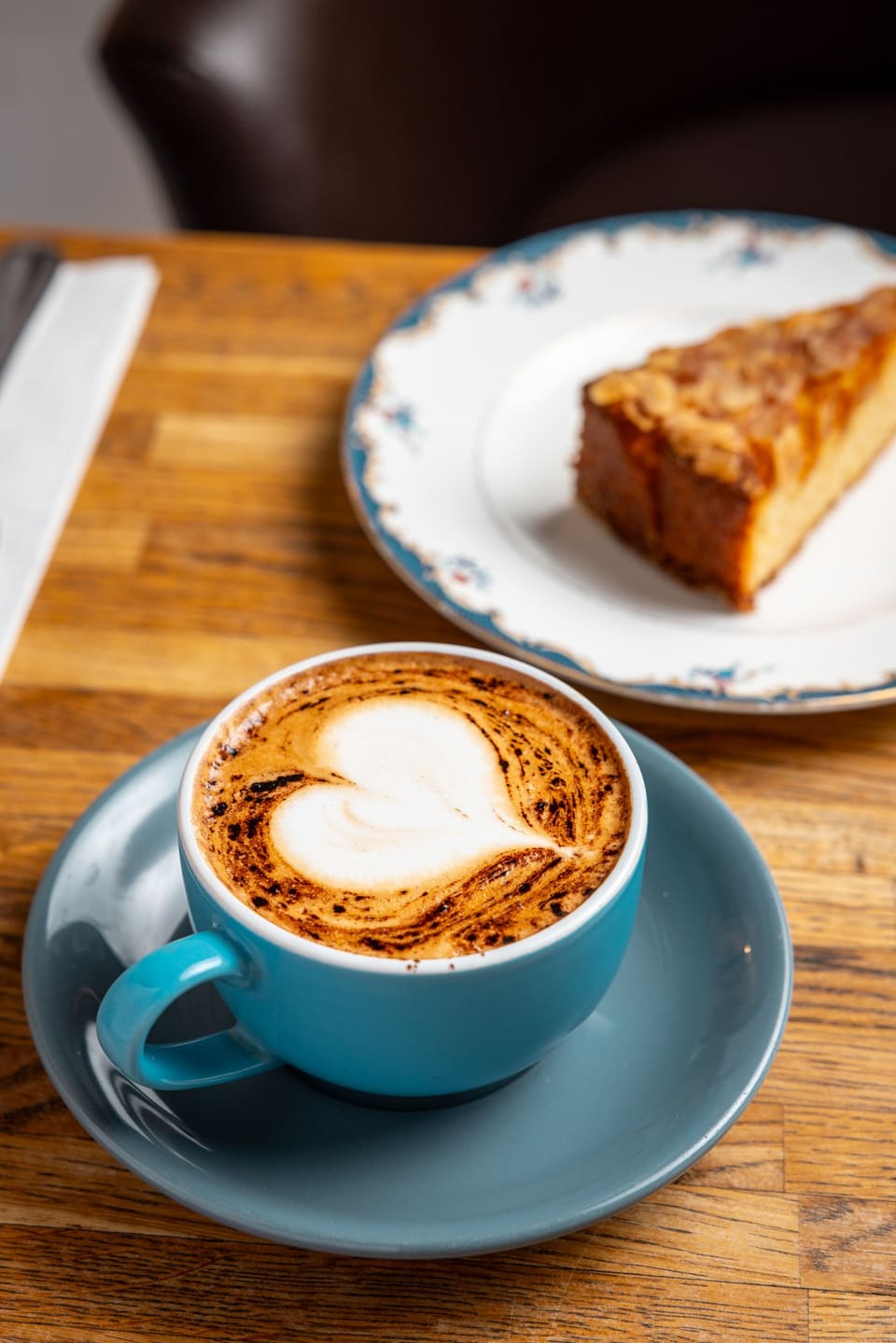 A latte with heart latte art beside a slice of almond cake