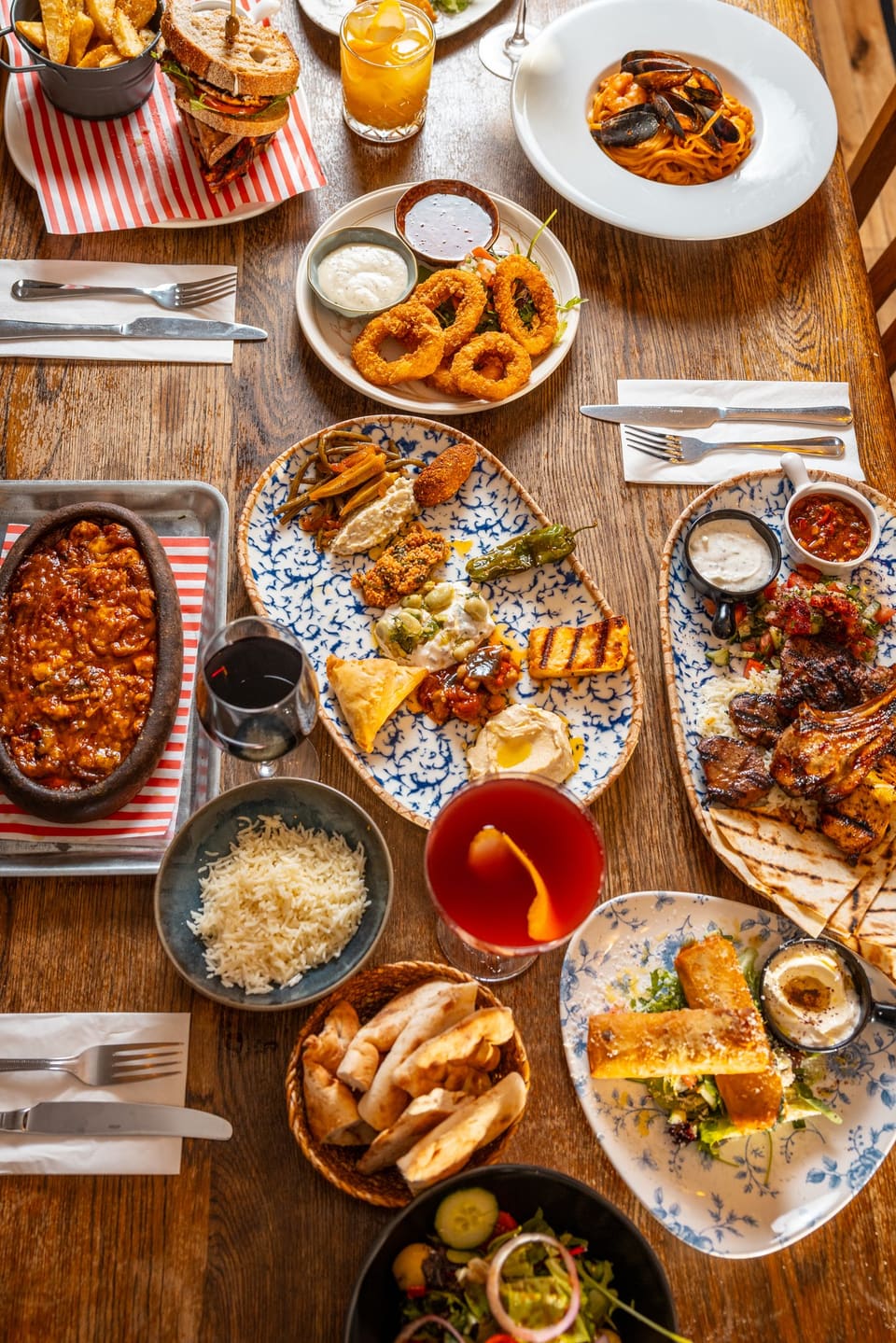 Overhead view of a table full of dishes: calamari, meze, grills, casserole, linguine and cocktails