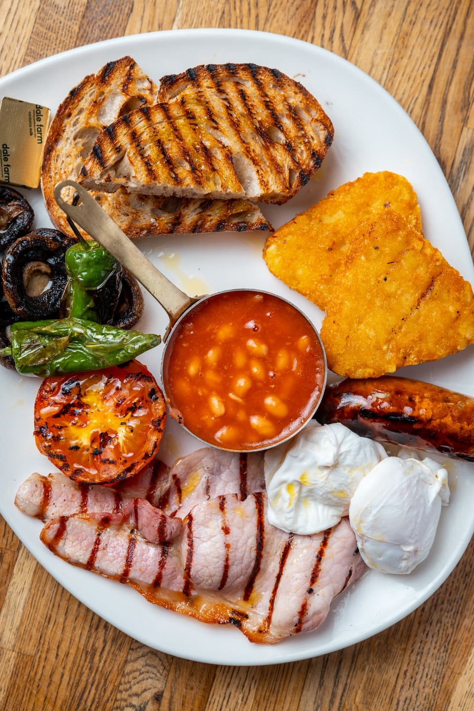 A Full English breakfast with bacon, hash brown, beans in a copper pot and poached eggs
