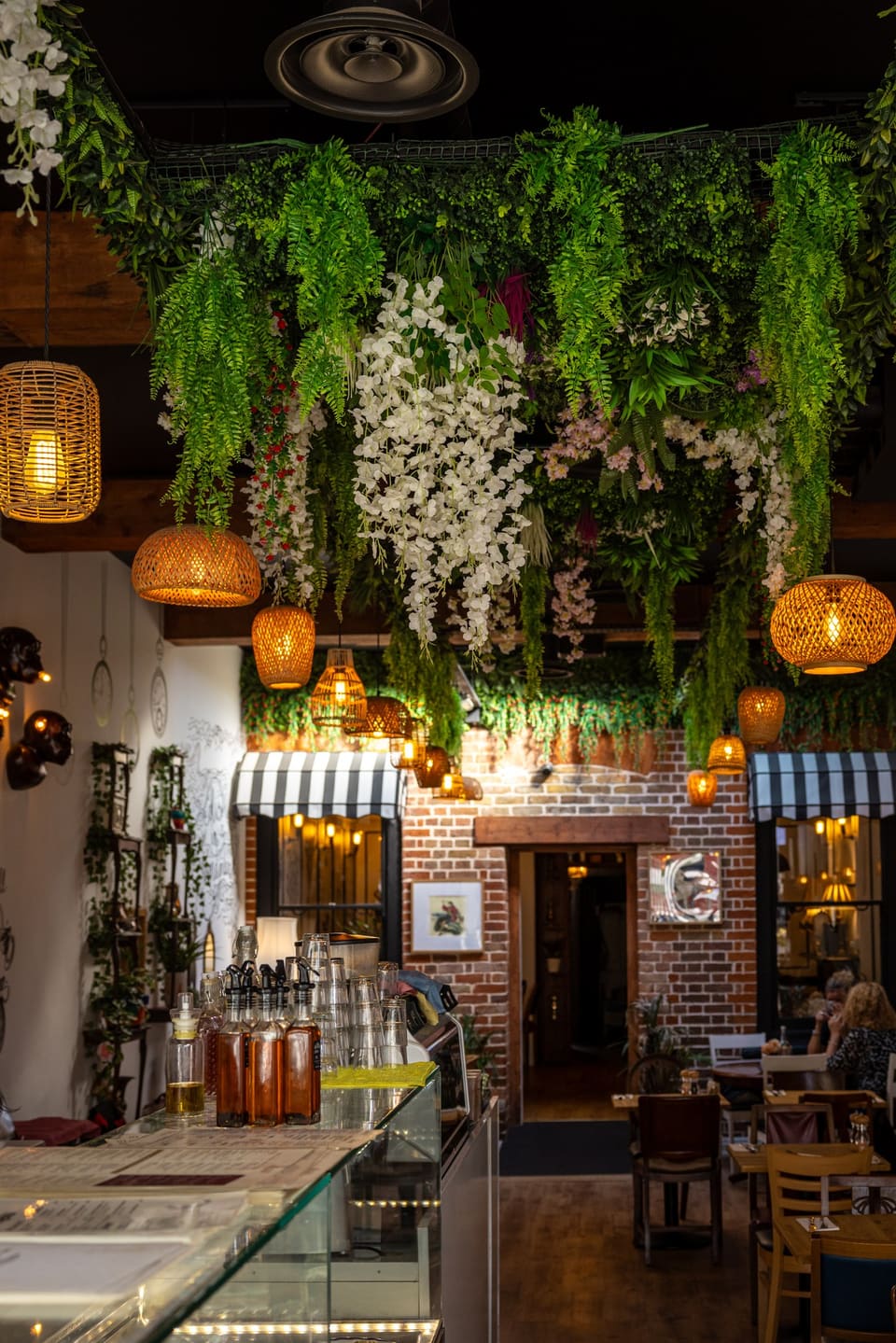 The Mad & Chef dining room: a ceiling of hanging foliage and white flowers, rattan lanterns and the striped awning over the counter
