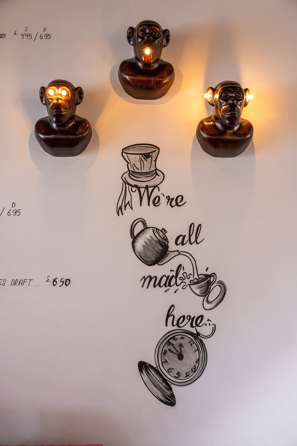 Wall lettering reading “We’re all mad here” beside bronze monkey wall lamps