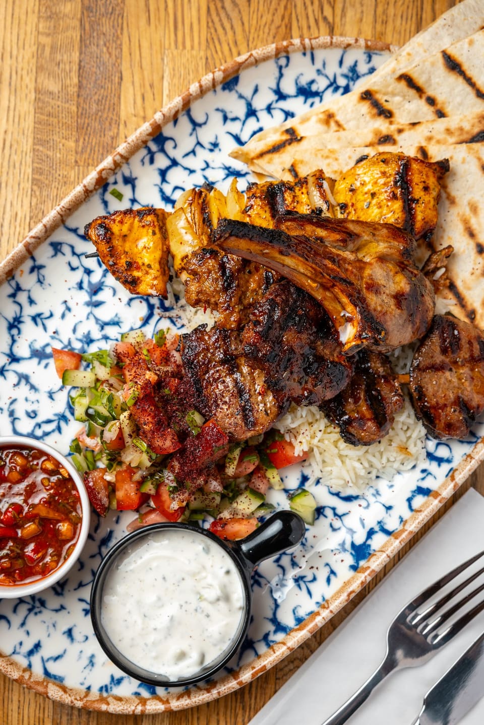 Mix grill of lamb chops, köfte and chicken on a blue patterned platter with grilled flatbread