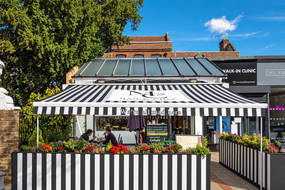 The Mad & Chef terrace under a black-and-white striped awning, with planters of red flowers and a blue sky