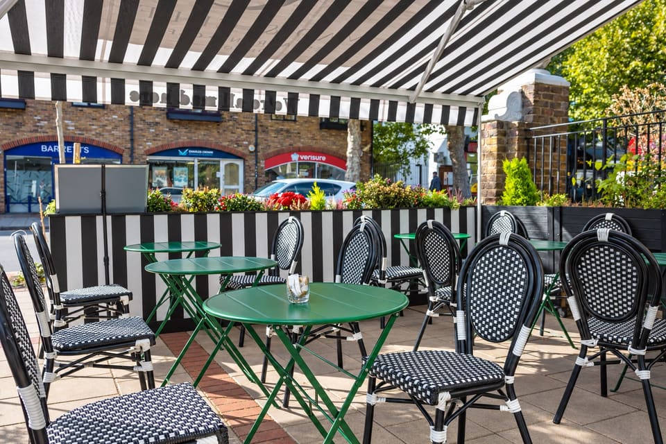 Green bistro tables and black-and-white chairs on the terrace under the striped awning